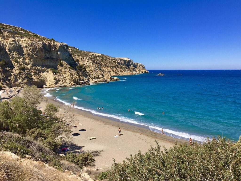 Best Sandy Beaches in Crete - 10. Kommos Beach Photo. ## **Kommos Beach: A Tranquil and Historic Destination in Crete**

**Kommos Beach** is located on the southern coast of **Crete**, near the village of **Matala** in the **Heraklion** region. Known for its quiet, relaxed atmosphere and stunning natural beauty, Kommos Beach offers a serene escape from the busier tourist spots on the island. This beach is also historically significant, with ruins from an ancient Minoan harbor nearby, making it an ideal destination for those seeking both natural beauty and cultural history.

### **Why Kommos Beach is Famous**

Kommos Beach is famous for its combination of natural charm and historical interest. The beach is surrounded by rocky cliffs, golden sand, and crystal-clear waters, making it a perfect place for swimming, sunbathing, and relaxation. The area is less developed than other beaches on the island, providing a more peaceful and secluded environment.

What makes Kommos especially unique is its proximity to the ruins of the **Minoan harbor** of Kommos, which was an important port during the **Minoan period** (around 2000 BC). These ruins are located on the nearby hills and can be visited as part of a walk to the beach. The site offers a fascinating glimpse into the island's ancient past and adds a historical dimension to the beach experience.

### **The Best Activities at Kommos Beach**

1. **Swimming and Sunbathing**: Kommos Beach is known for its pristine, clear waters, making it an excellent spot for swimming. The beach is relatively uncrowded, offering plenty of space for sunbathing and relaxing. The shallow waters are calm, which makes it suitable for families, while the deeper parts offer a refreshing swim for adults.

2. **Exploring the Minoan Ruins**: A short walk from the beach leads to the **archaeological site of Kommos**, where you can explore the ruins of the ancient harbor, docks, and Minoan buildings. The ruins are not as widely visited as other archaeological sites in Crete, so you can enjoy a quieter and more intimate experience. The site offers breathtaking views of the coastline and the surrounding landscape, making it a must-see for history enthusiasts.

3. **Hiking and Nature Walks**: The area surrounding Kommos Beach is perfect for outdoor enthusiasts. You can enjoy scenic hikes along the cliffs or explore the surrounding countryside. The landscape features diverse flora and fauna, offering a peaceful setting for nature walks.

4. **Photography**: With its dramatic backdrop of cliffs, clear waters, and historical ruins, Kommos Beach is a photographer’s paradise. Whether you're capturing the natural beauty of the beach, the ancient Minoan structures, or the stunning sunsets, there are endless opportunities for memorable photographs.

5. **Camping**: Kommos Beach is one of the few places in Crete where camping is allowed directly on the beach. The beach has a more rustic feel compared to other areas, and camping here offers a chance to fully immerse yourself in nature, with the sound of the waves and the starry sky above.

### **How to Get to Kommos Beach**

1. **From Heraklion**: Kommos Beach is located about **70 kilometers south of Heraklion** city. The drive takes around **1.5 to 2 hours**. To reach the beach, take the **E70 road** toward the town of **Moires**, and then follow signs for **Matala**. From Matala, the beach is a short drive or a 10-minute walk away.

2. **From Matala**: The beach is located just outside the village of **Matala**. If you’re staying in Matala, you can easily walk or take a short drive to Kommos Beach. The beach is a few kilometers from the village center, and the path is well-marked.

3. **Public Transport**: There are buses from **Heraklion** to **Matala**, and from there you can either walk or take a short taxi ride to Kommos Beach. However, public transport options to the beach directly are limited, so it is recommended to travel by car or taxi for convenience.

4. **Parking**: There is parking available near the beach, although it can get busier during peak tourist season. Arriving early will give you a better chance of securing a spot.

### **Best Time to Visit Kommos Beach**

The best time to visit Kommos Beach is during the **spring (April to June)** and **early autumn (September to October)** when the weather is warm, and the beach is less crowded. The summer months (July and August) can bring more tourists, but the beach still maintains a peaceful atmosphere due to its secluded location. To avoid crowds, it’s best to visit early in the morning or later in the evening.

### **Conclusion**

**Kommos Beach** offers a unique combination of natural beauty, peaceful surroundings, and historical intrigue. Its golden sands and clear waters are perfect for relaxation, while the nearby **Minoan ruins** provide an enriching cultural experience. Whether you're a history enthusiast, nature lover, or just looking to unwind by the sea, Kommos Beach is a hidden gem that showcases the best of Crete’s charm and serenity.